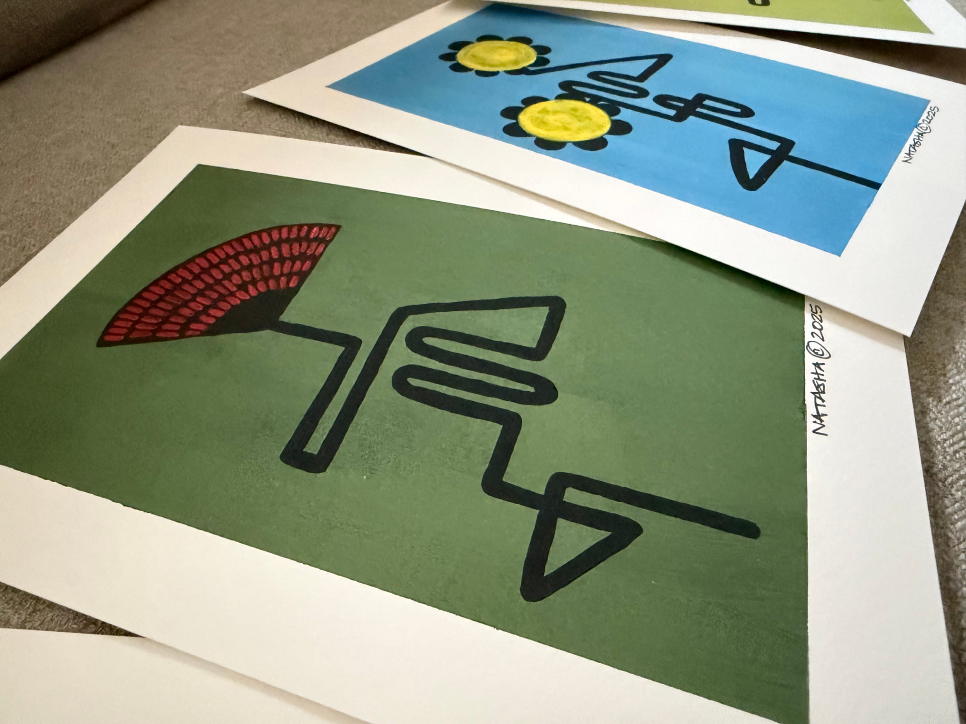 Hand-painted botanical art prints resting on a woven neutral surface